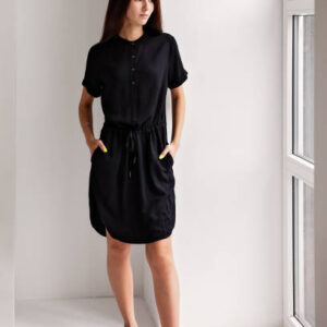 A young girl in a black dress stands in the room by the window